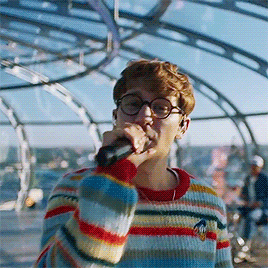 A Man Singing Into A Microphone Wearing A Striped Sweater GIF