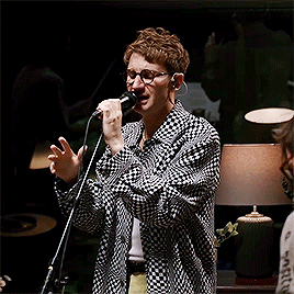A Man Singing Into A Microphone Wearing Glasses And A Plaid Shirt GIF