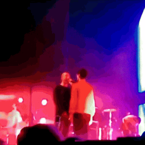 A Man Singing Into A Microphone While Another Man Looks On GIF