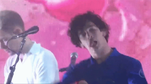 A Man Singing Into A Microphone While Another Man Looks On GIF