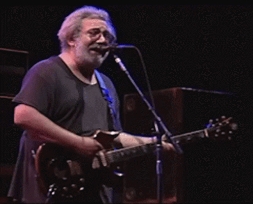 A Man Singing Into A Microphone While Holding A Guitar GIF