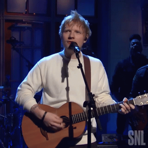 A Man Singing Into A Microphone While Holding A Guitar That Says Snl GIF