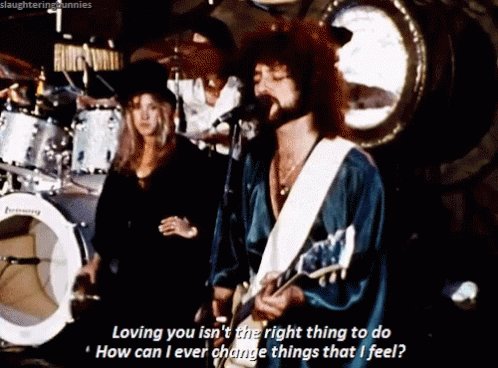 A Man Singing Into A Microphone While Playing A Guitar And A Woman Stands Behind Him GIF