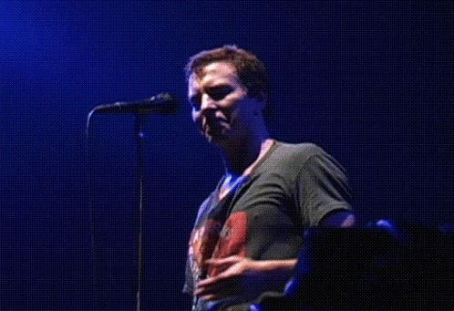a man singing into a microphone while wearing a shirt that says ' the rolling stones ' on it