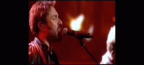 a man singing into a microphone with a guitar in the background
