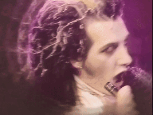 A Man Singing Into A Microphone With Purple Hair GIF