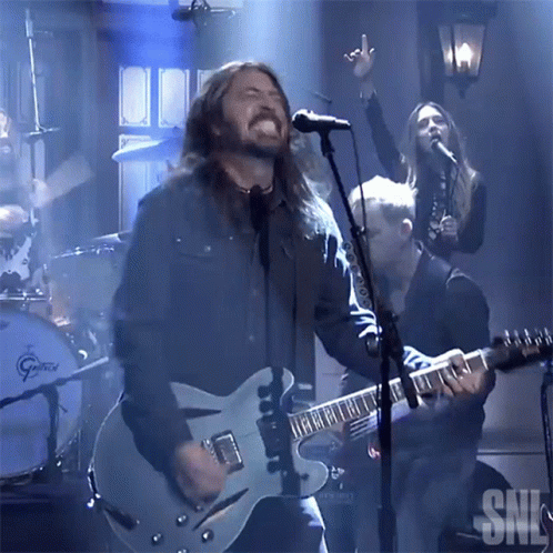 A Man Singing Into A Microphone With The Letters Snl Visible In The Background GIF