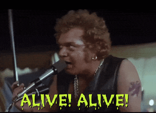 A Man Singing Into A Microphone With The Words Alive Alive Written On The Screen GIF
