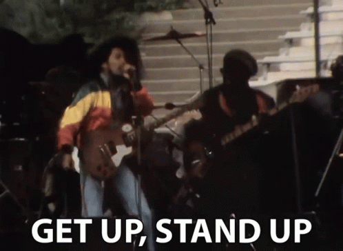 A Man Singing Into A Microphone With The Words " Get Up Stand Up " Next To Him GIF