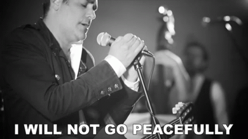 A Man Singing Into A Microphone With The Words " I Will Not Go Peacefully " Next To Him GIF