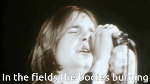 A Man Singing Into A Microphone With The Words In The Fields The Bodies Burning Above Him . GIF