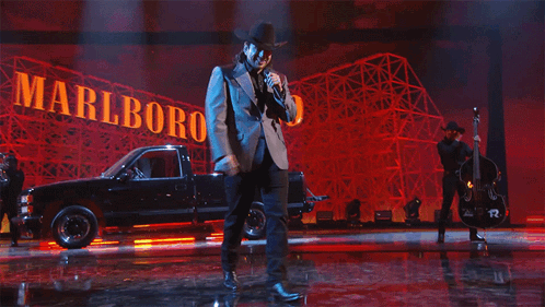 A Man Singing On Stage In Front Of A Sign That Says Marlboro GIF