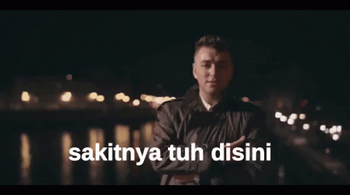 A Man Singing With The Words Sakitnya Tuh Disini Written Below Him GIF