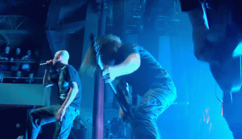 A Man Sings Into A Microphone While Another Man Holds A Guitar GIF