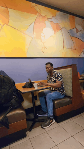 A Man Sits At A Booth In A Restaurant Using A Laptop GIF