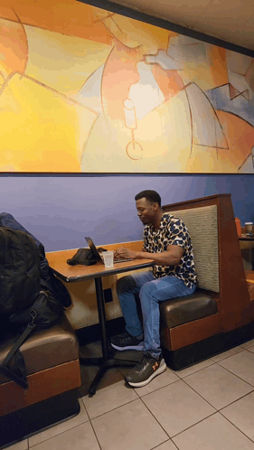 A Man Sits At A Booth In A Restaurant Using His Laptop GIF