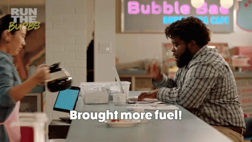 A Man Sits At A Counter In Front Of A Sign That Says Bubble Day GIF