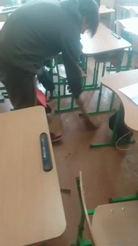 A Man Sits At A Desk In A Classroom With A Cell Phone In His Hand GIF