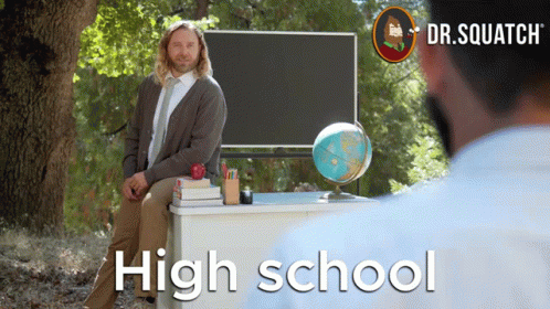 A Man Sits At A Desk In Front Of A Blackboard With The Words High School On It GIF