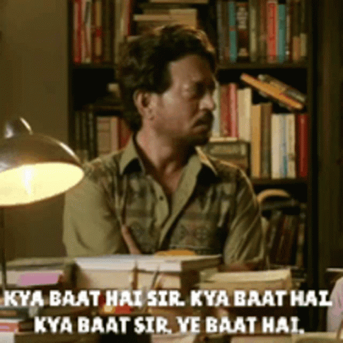 A Man Sits At A Desk In Front Of A Bookshelf With The Words Kya Baat Hai Sir Written On The Bottom GIF