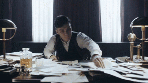 A Man Sits At A Desk With A Bottle Of Whiskey On It GIF