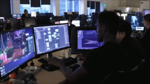 A Man Sits At A Desk With A Computer Monitor Displaying A Game GIF