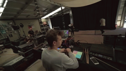 A Man Sits At A Desk With A Keyboard And A Phone In Front Of A Monitor That Says ' Korg ' On It GIF