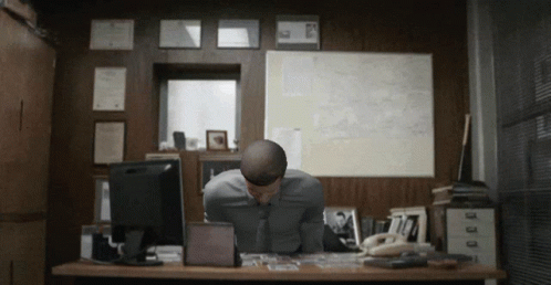 A Man Sits At A Desk With His Head Down In Front Of A Computer GIF
