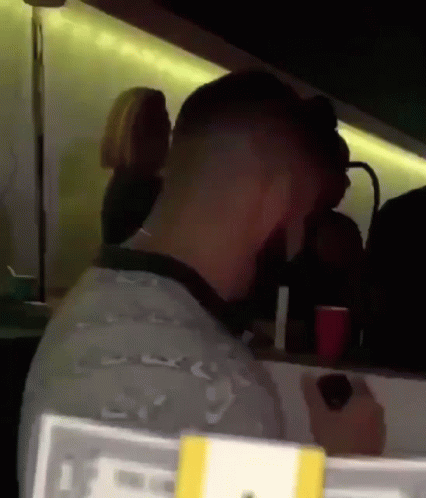 A Man Sits At A Table In A Dark Room With A Sign That Says ' Lg ' On It GIF