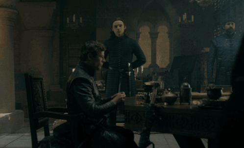 A Man Sits At A Table In A Dark Room With Candles GIF