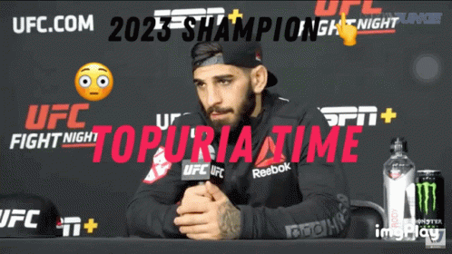 A Man Sits At A Table In Front Of A Ufc Fight Night Poster GIF