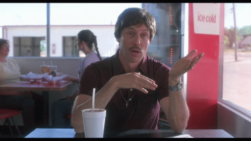 A Man Sits At A Table In Front Of An Ice Cold Drink Machine GIF