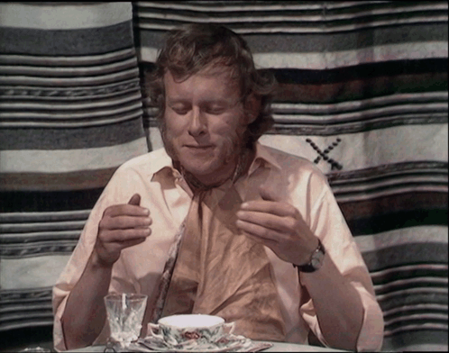 A Man Sits At A Table With A Cup Of Tea GIF