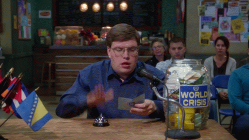 A Man Sits At A Table With A Jar That Says World Crisis On It GIF