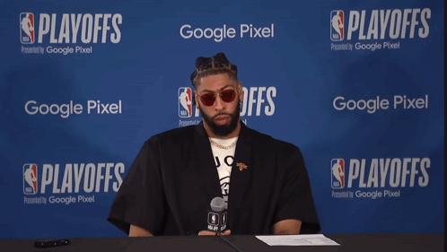 A Man Sits At A Table With A Microphone In Front Of A Google Pixel Banner GIF