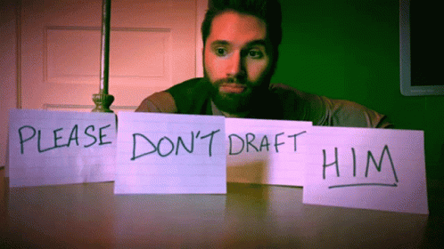 A Man Sits At A Table With A Sign That Says Please Do N't Draft Him GIF