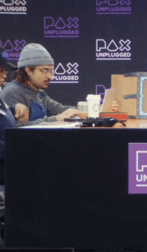 A Man Sits At A Table With A Watch Out Sign In Front Of Him GIF