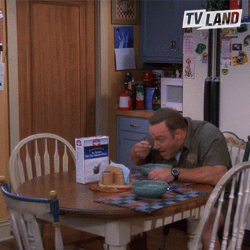 A Man Sits At A Table With Bowls Of Food Under A Tv Land Banner GIF