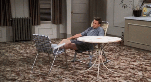 A Man Sits At A Table With His Feet On The Table GIF