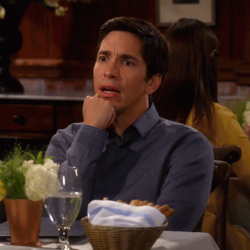 A Man Sits At A Table With His Hand On His Chin GIF