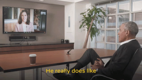a man sits at a table with his legs crossed and says he really does like while watching a tv