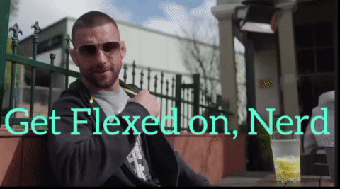 A Man Sits At A Table With The Words Get Flexed On Nerd GIF