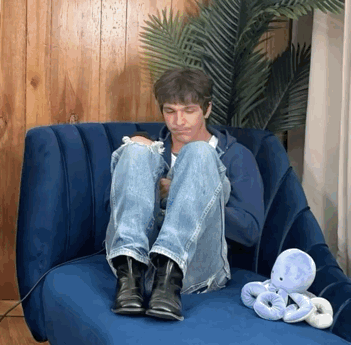 a man sits in a blue chair with his legs crossed