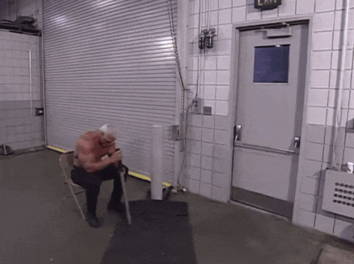 A Man Sits In A Chair In Front Of A Door That Has An Exit Sign On It GIF