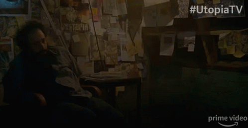 A Man Sits In A Chair In Front Of A Wall With Papers On It And The Words Utopia Tv On The Bottom GIF