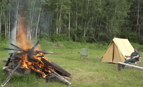 A Man Sits In A Chair Near A Campfire GIF