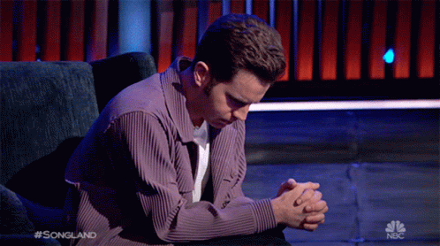 A Man Sits In A Chair With His Hands Folded In Prayer On A Nbc Show GIF