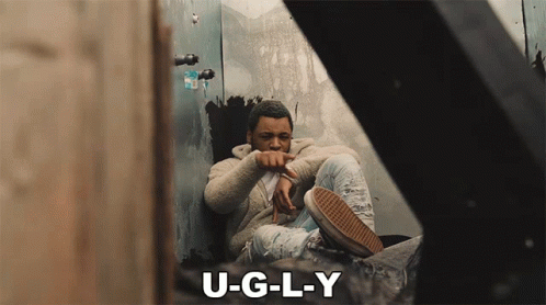 A Man Sits In A Corner With The Words U-G-L-Y Below Him GIF