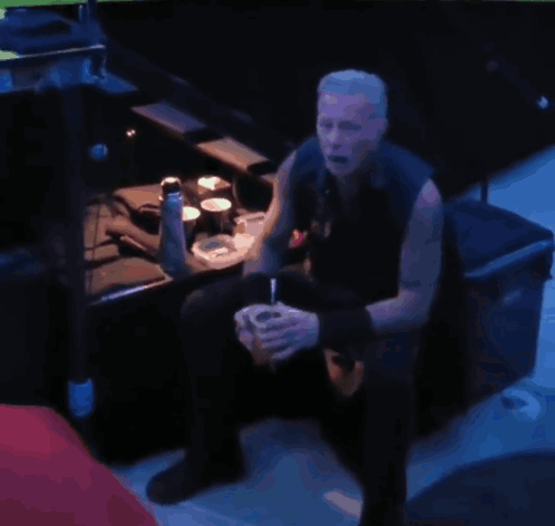 A Man Sits In A Dark Room Drinking From A Cup GIF