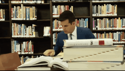 A Man Sits In A Library Surrounded By Books Including One Titled Shakespeare 8 GIF